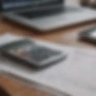 Close-up of a calculator and budgeting sheets with a MacBook nearby